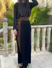 Person wearing a black outfit with floral embroidery standing on a balcony.